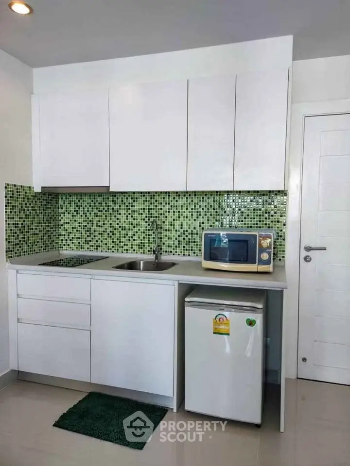 Modern compact kitchen with white cabinets and green mosaic backsplash, featuring a microwave and mini fridge.