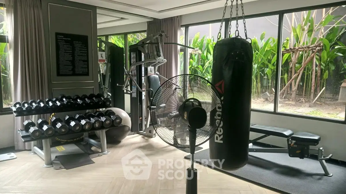 Modern home gym with punching bag, weights, and exercise equipment in a bright room with large windows.