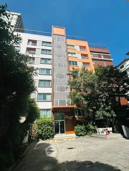 Modern multi-story building with vibrant facade and lush greenery in urban setting.