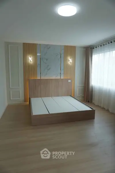 Spacious modern bedroom with elegant wooden paneling and large window for natural light.