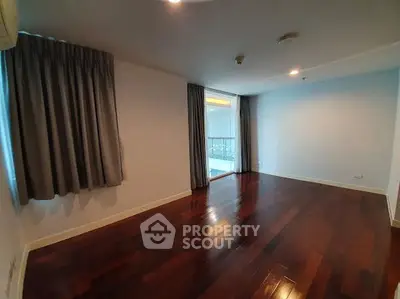 Spacious empty room with wooden flooring and large windows in modern apartment.
