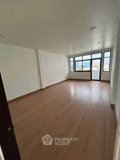 Spacious empty room with large windows and wooden flooring, ideal for customization.