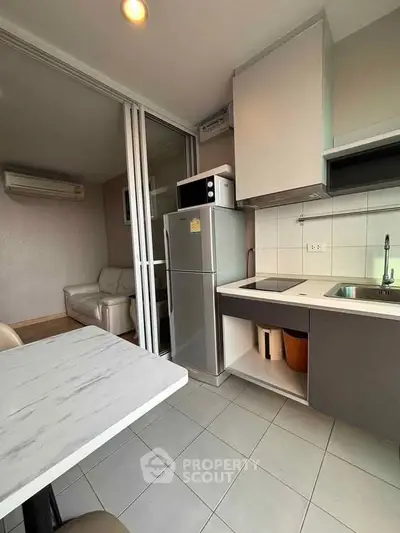 Modern kitchen with sleek appliances and cozy living area in open layout apartment.