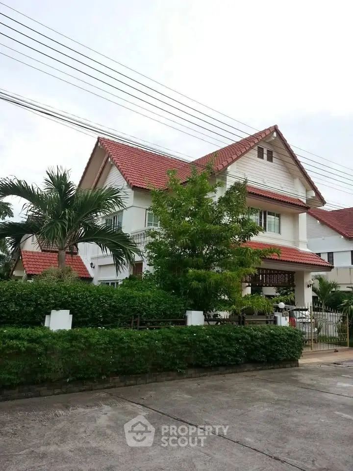 Charming two-story house with red roof and lush greenery in a serene neighborhood.