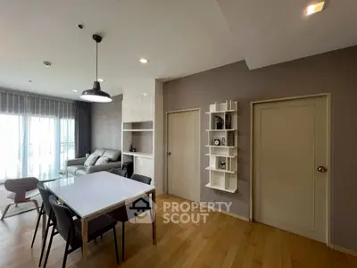 Modern living room with dining area, featuring sleek furniture and natural light from large windows.