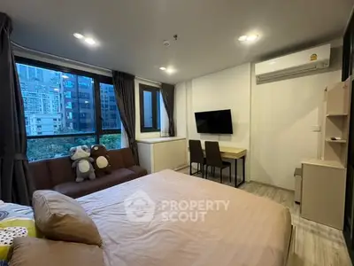 Modern bedroom with city view, cozy sofa, and wall-mounted TV in urban apartment.