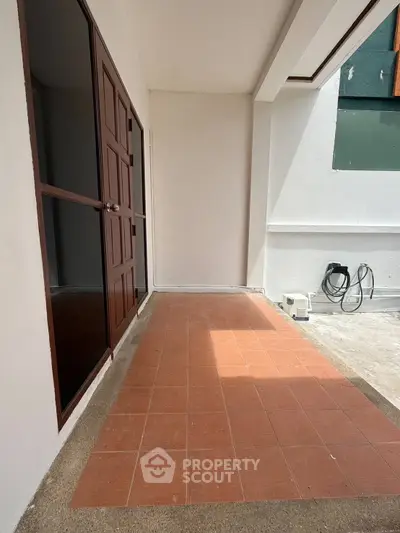 Spacious balcony with tiled flooring and wooden door, perfect for outdoor relaxation.