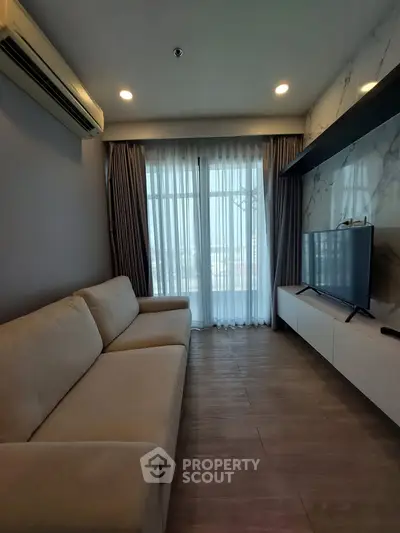 Modern living room with large window, sleek TV setup, and cozy beige sofa.