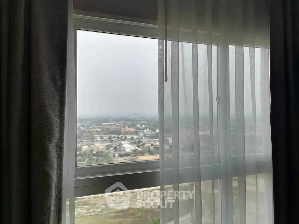 Stunning cityscape view from a high-rise apartment window with sheer curtains.