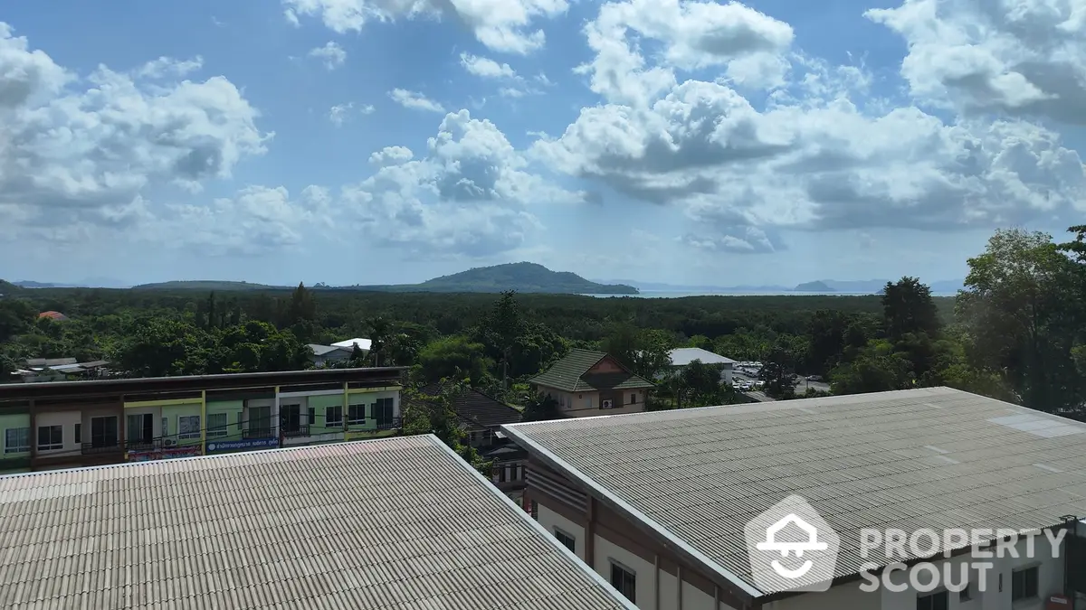 Expansive view from a property showcasing a serene mountainous horizon beyond urban rooftops under a sky dotted with fluffy clouds.