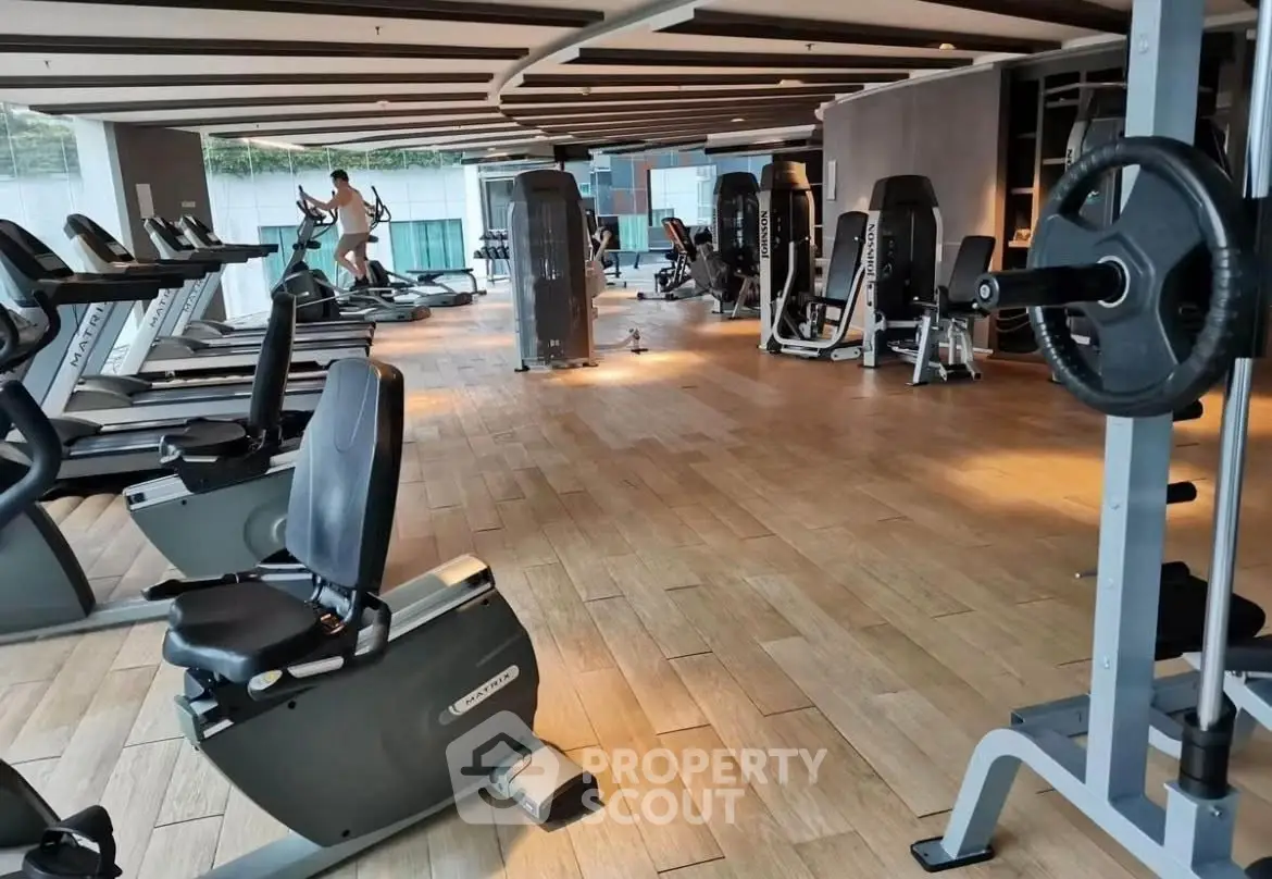 Spacious modern gym with state-of-the-art equipment and wooden flooring in luxury residential building.