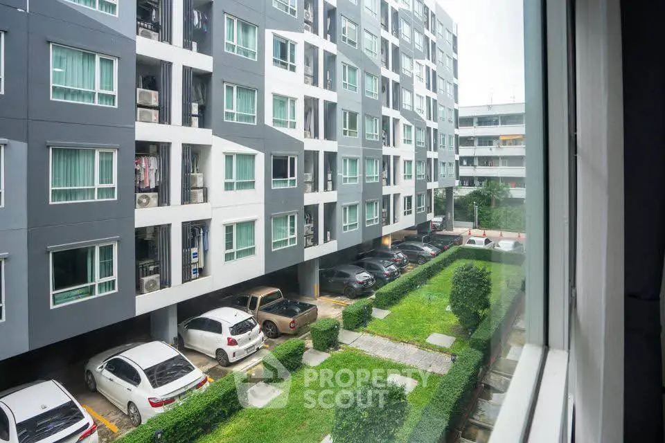Modern apartment building with parking and green courtyard view from window.