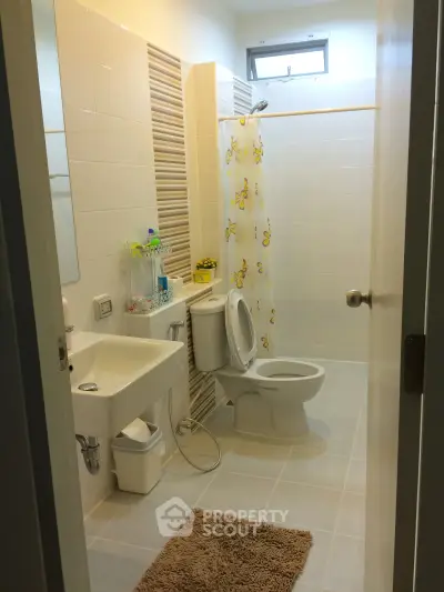 Modern bathroom with shower curtain, sink, and toilet in a bright, tiled space.
