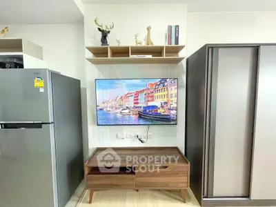 Modern living room with sleek furniture and mounted TV, featuring stylish decor and a stainless steel fridge.