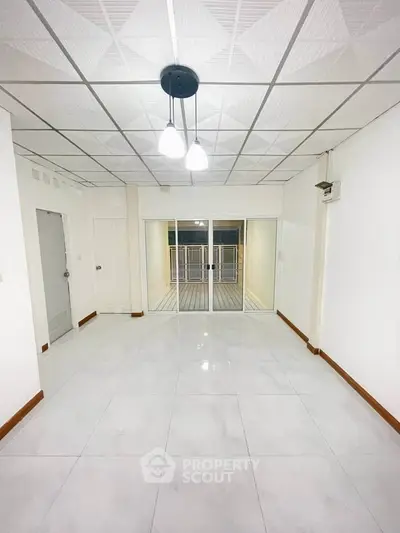 Spacious white-tiled room with modern lighting and sliding glass doors leading to a balcony.