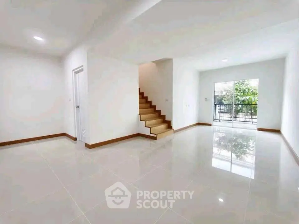 Spacious modern living room with glossy tile flooring and staircase, leading to a bright balcony view.