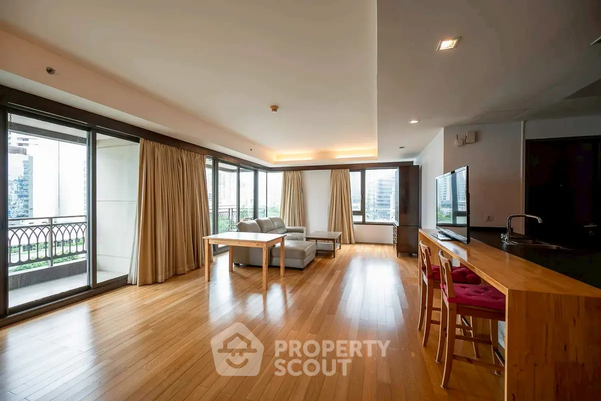 Spacious modern living room with hardwood floors and large windows offering city views.