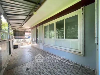 Spacious covered balcony with tiled flooring and large windows in a serene setting.