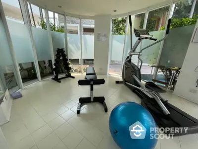 Modern home gym with treadmill, weights, and exercise ball in bright room