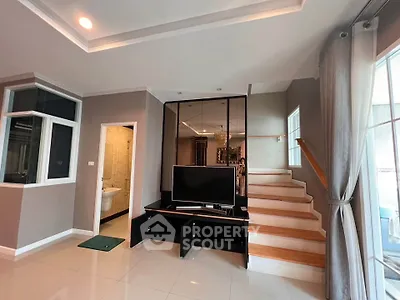 Modern living room with staircase and TV, featuring sleek design and natural light.