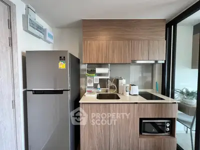 Modern compact kitchen with sleek wooden cabinets and stainless steel appliances in a stylish apartment.