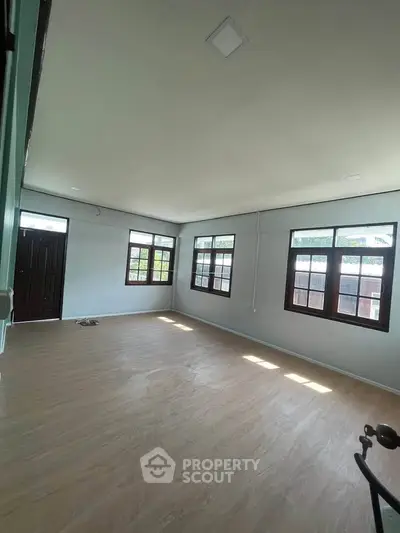 Spacious empty room with large windows and wooden flooring, ideal for customization.