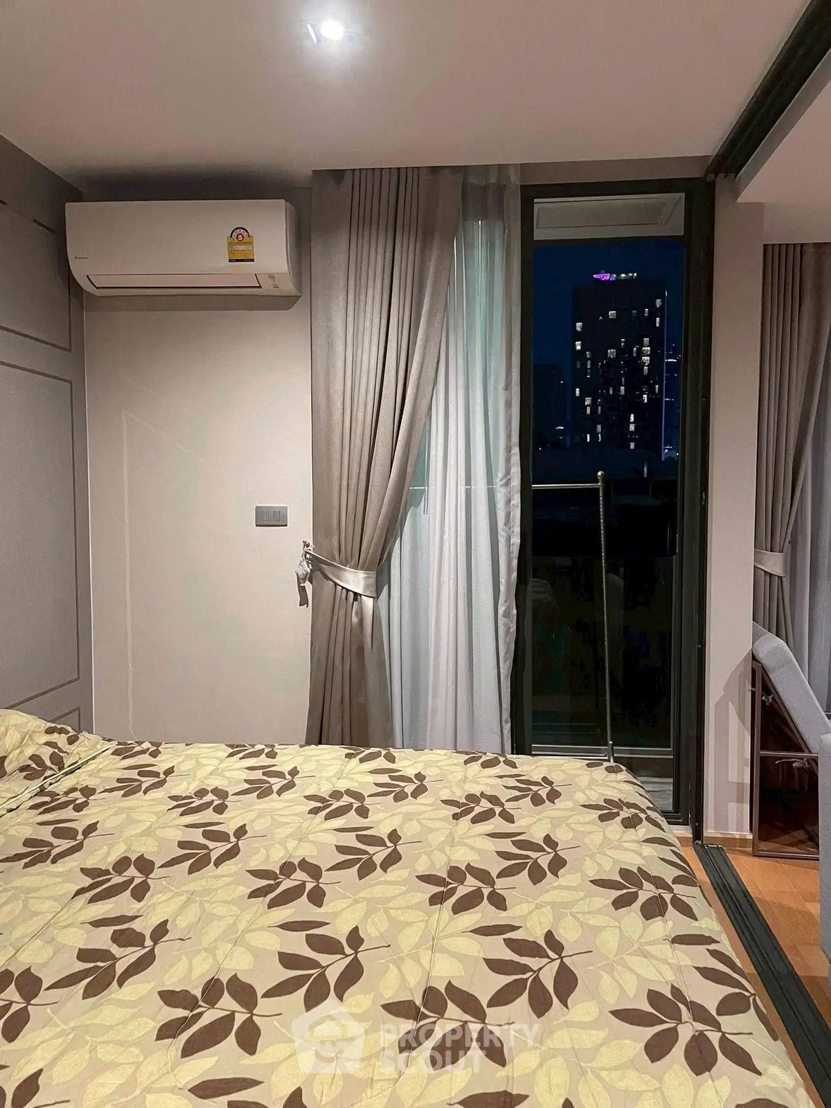 Cozy bedroom with balcony access and city view, featuring air conditioning and elegant curtains.