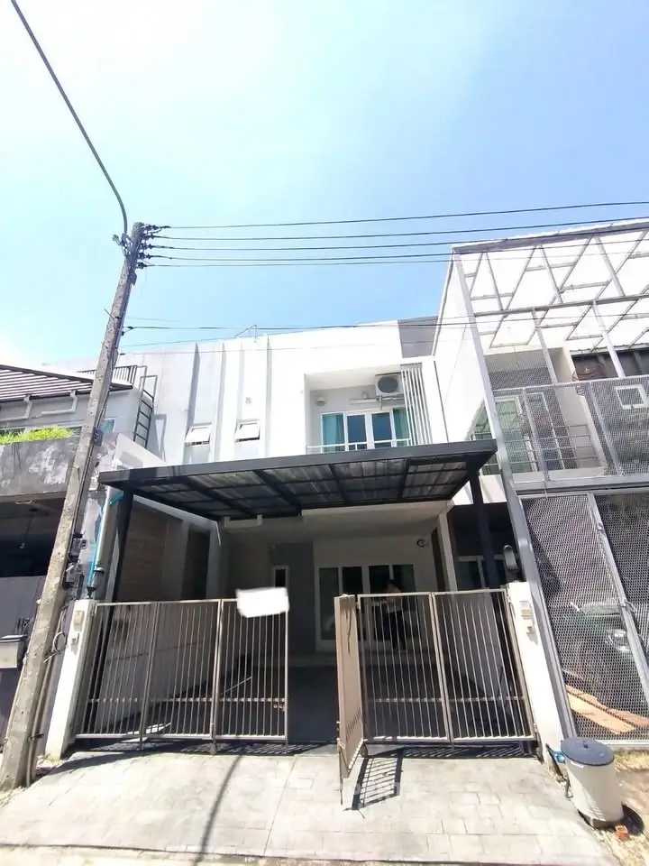 Modern townhouse exterior with gated entrance and carport under clear blue sky.