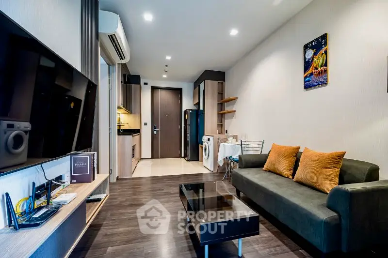 Modern living room with sleek dark wood flooring, comfortable sofa, and a well-equipped kitchen in the background, perfect for urban living.