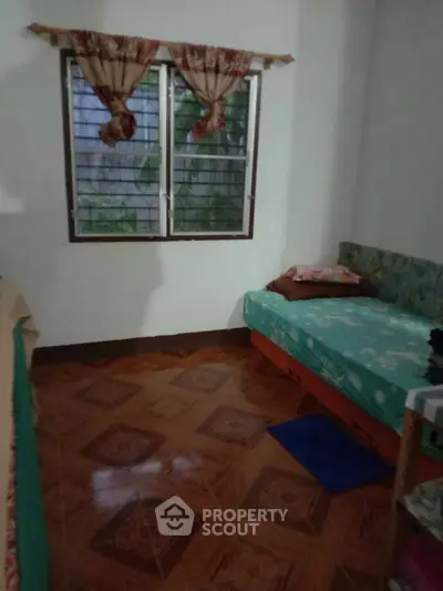 Cozy bedroom with single bed and window view, featuring patterned floor tiles and simple decor.