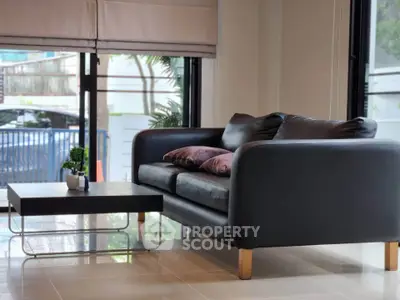 Modern living room with sleek black sofa and stylish coffee table, featuring large windows for natural light.