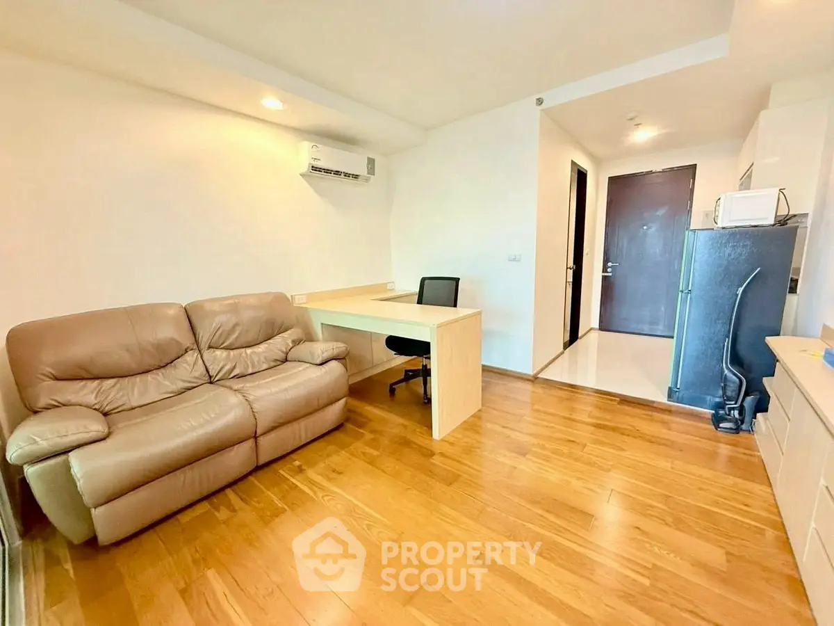 Modern living room with wooden flooring, leather sofa, and study desk in a cozy apartment.