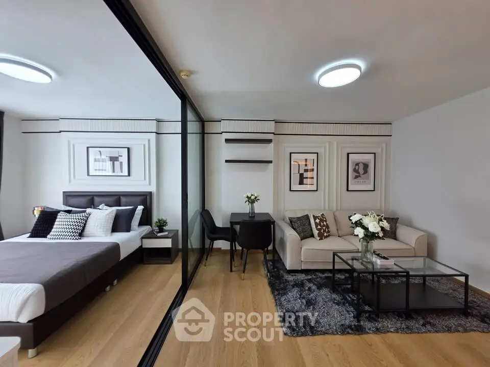 Modern studio apartment with stylish decor, featuring a cozy living area and elegant bedroom separated by glass partition.