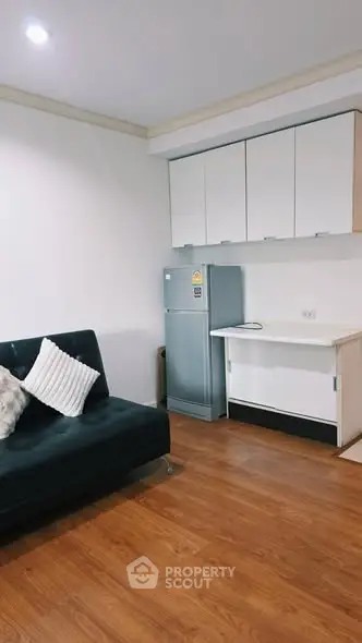 Modern living room with sleek sofa and compact kitchen area featuring a stainless steel fridge.