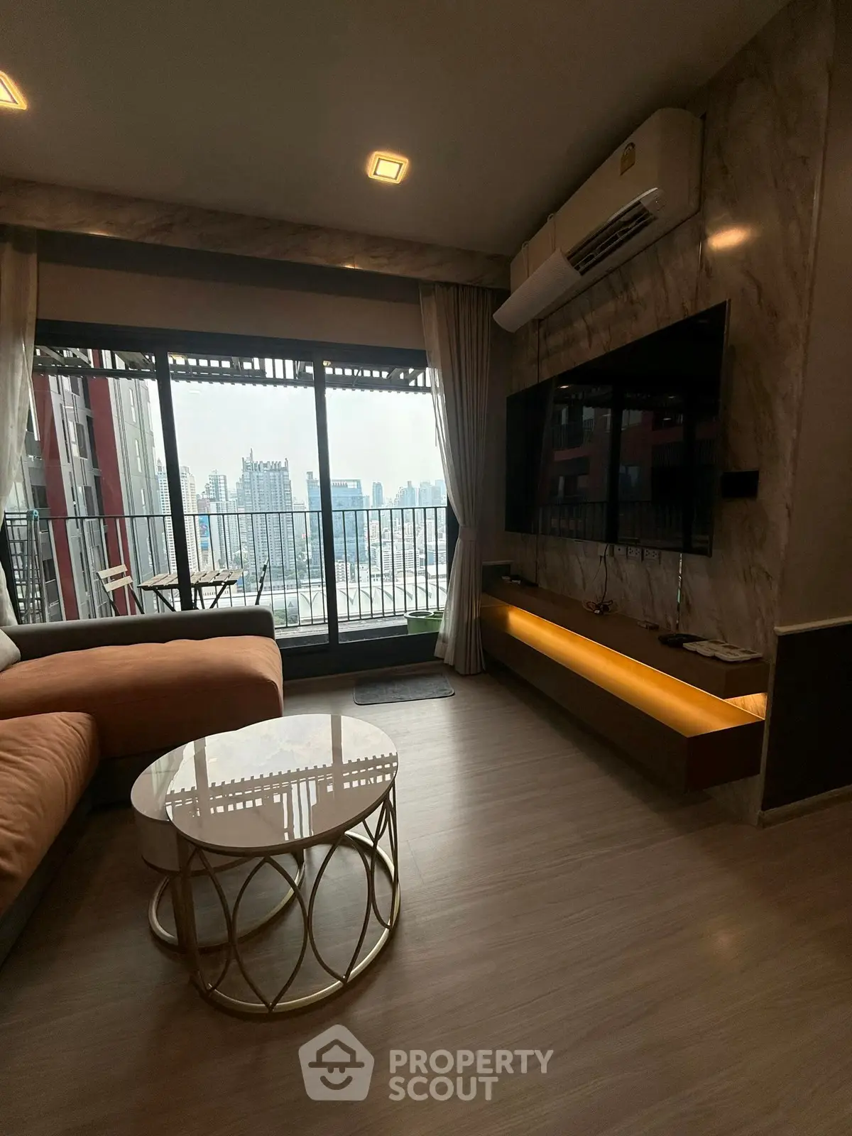 Modern living room with city view, featuring a large TV and stylish furniture.