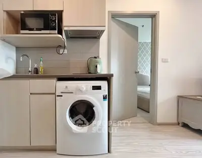 Modern kitchen with washing machine and microwave, open layout to cozy bedroom.