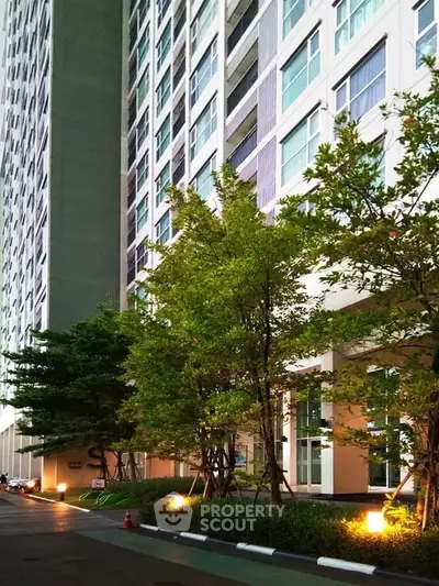 Modern high-rise building exterior with lush greenery and well-lit entrance