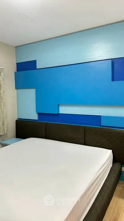 Modern bedroom with unique blue geometric wall design and cozy bed.
