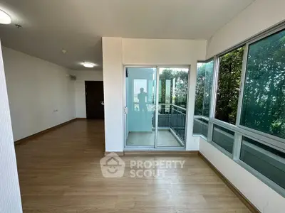 Spacious living room with large windows and balcony access, featuring modern wooden flooring.