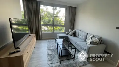 Spacious and modern living room with large windows offering ample natural light, featuring a comfortable grey sofa, stylish glass coffee table, and sleek entertainment unit.