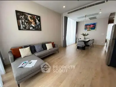 Modern living room with stylish decor and open dining area, featuring wooden flooring and contemporary artwork.