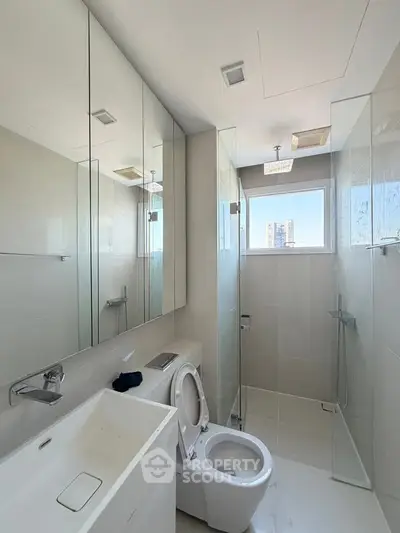 Modern bathroom with sleek fixtures and large mirrors, featuring a glass-enclosed shower and city view window.