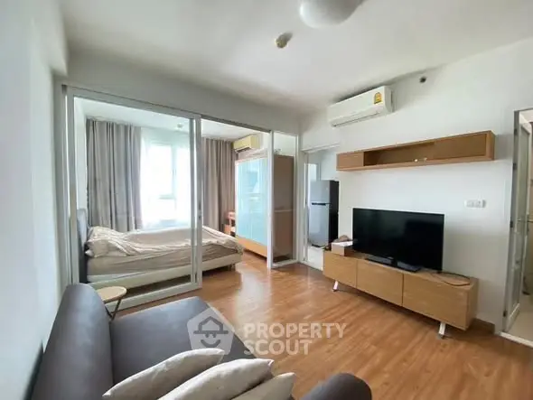 Modern apartment with open living room and bedroom, featuring sleek furniture and wooden flooring.