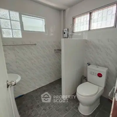 Modern bathroom with tiled walls and floor, featuring a toilet and natural light from windows.