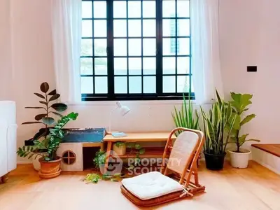 Charming living room with natural light, cozy seating, and lush indoor plants.