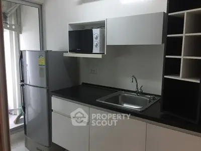 Modern kitchen with sleek cabinets, stainless steel fridge, and microwave.