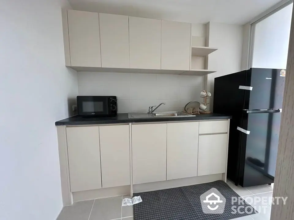 Modern kitchen with sleek cabinets and black fridge, featuring a microwave and ample counter space.