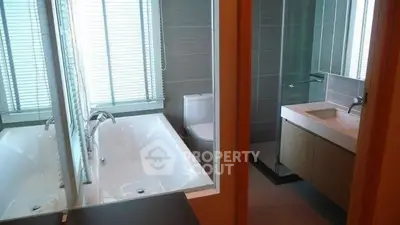 Modern bathroom with bathtub and sleek fixtures, featuring large mirror and natural light.