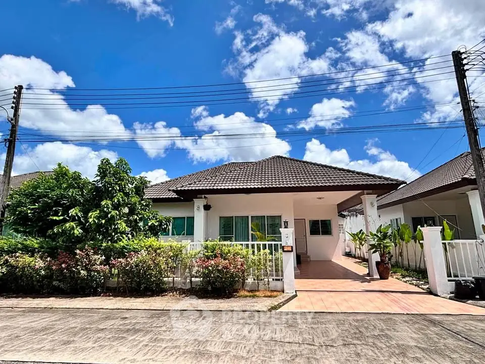 Charming single-story house with lush garden and spacious driveway under a clear blue sky.