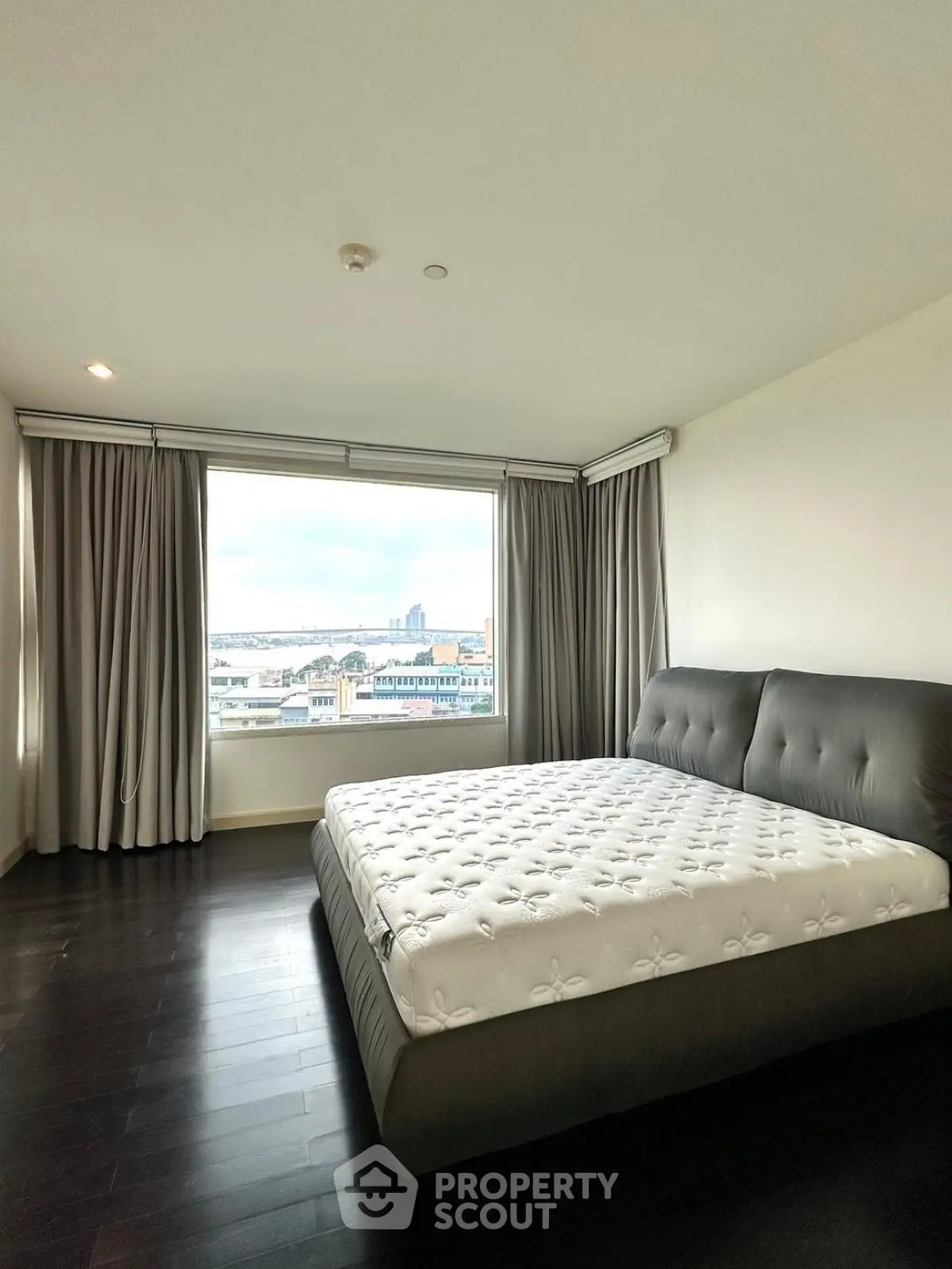 Spacious bedroom with large window offering stunning city view and elegant dark wood flooring.